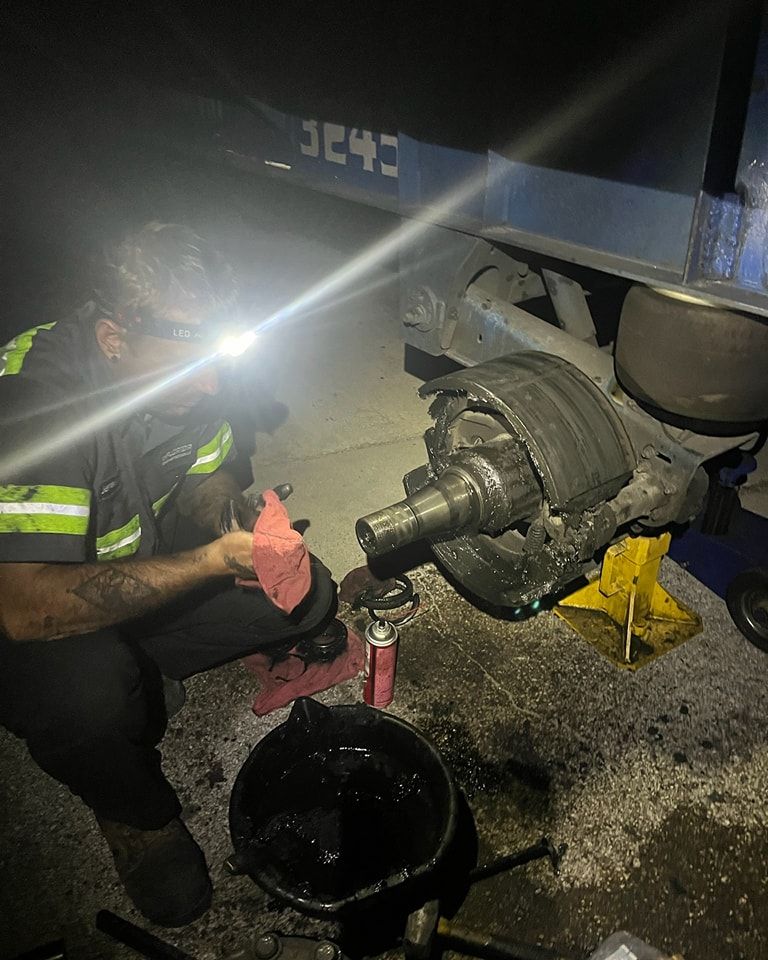 A man is working on a truck at night with a flashlight.