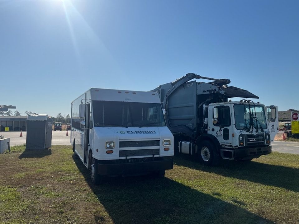 A bus and a garbage truck are parked next to each other in a grassy field.