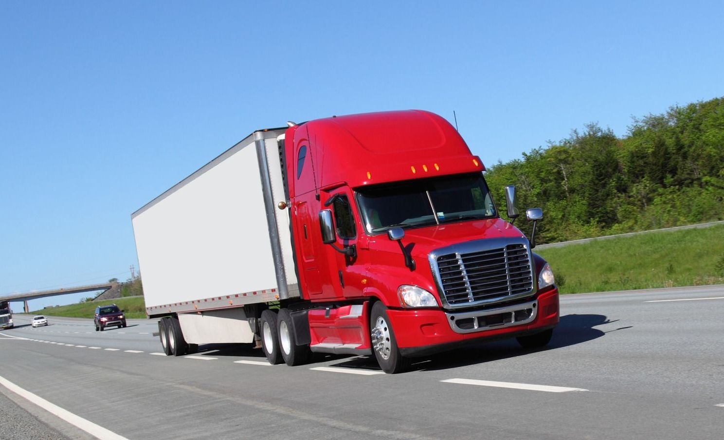 A red semi truck with a white trailer is driving down a highway.