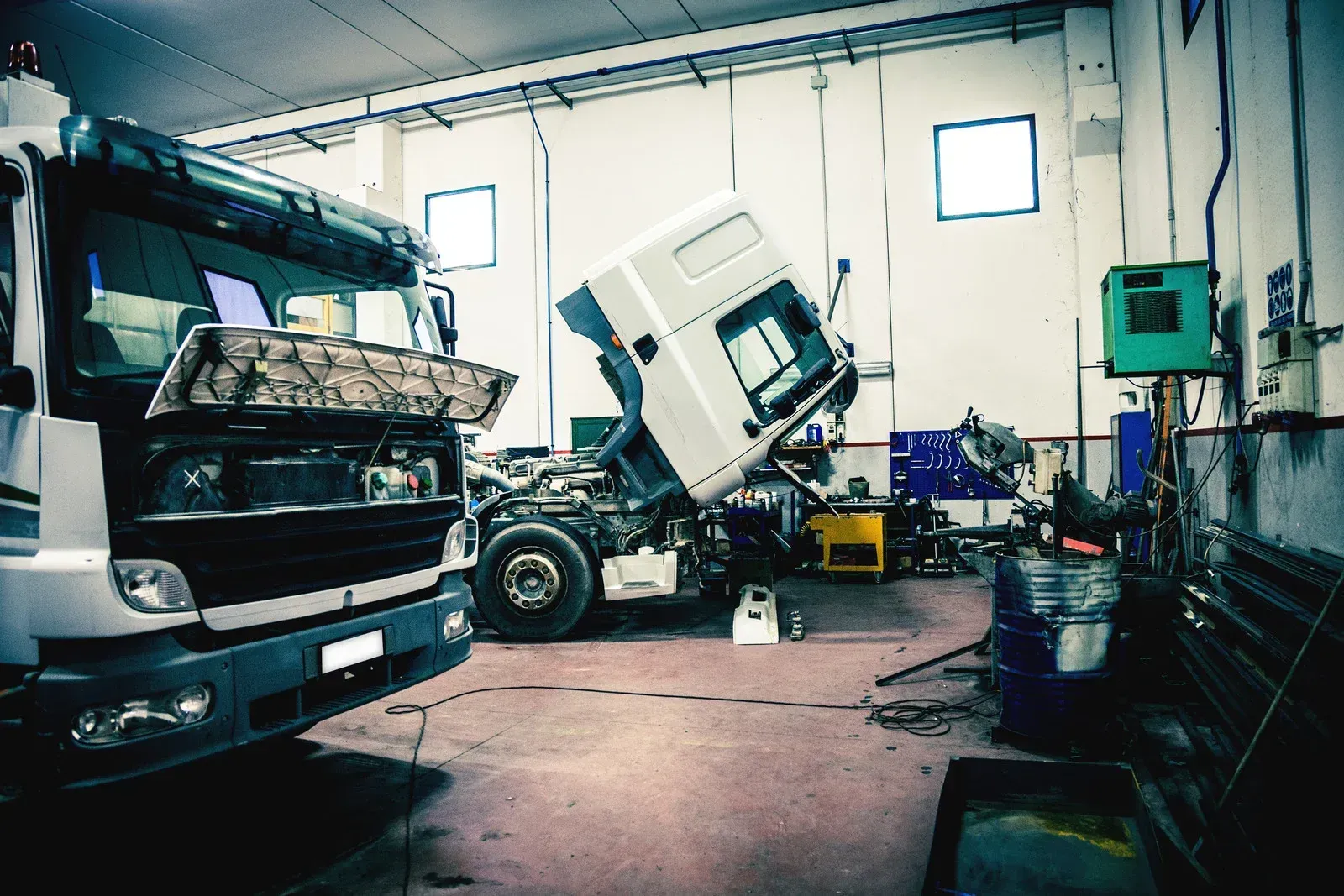 A truck is being repaired in a garage with its hood open.