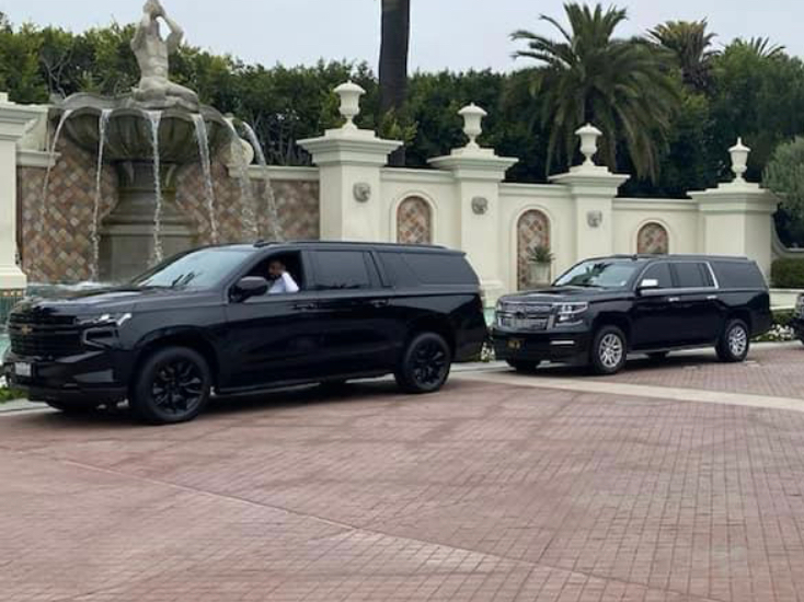 two black suvs are parked in front of a fountain .