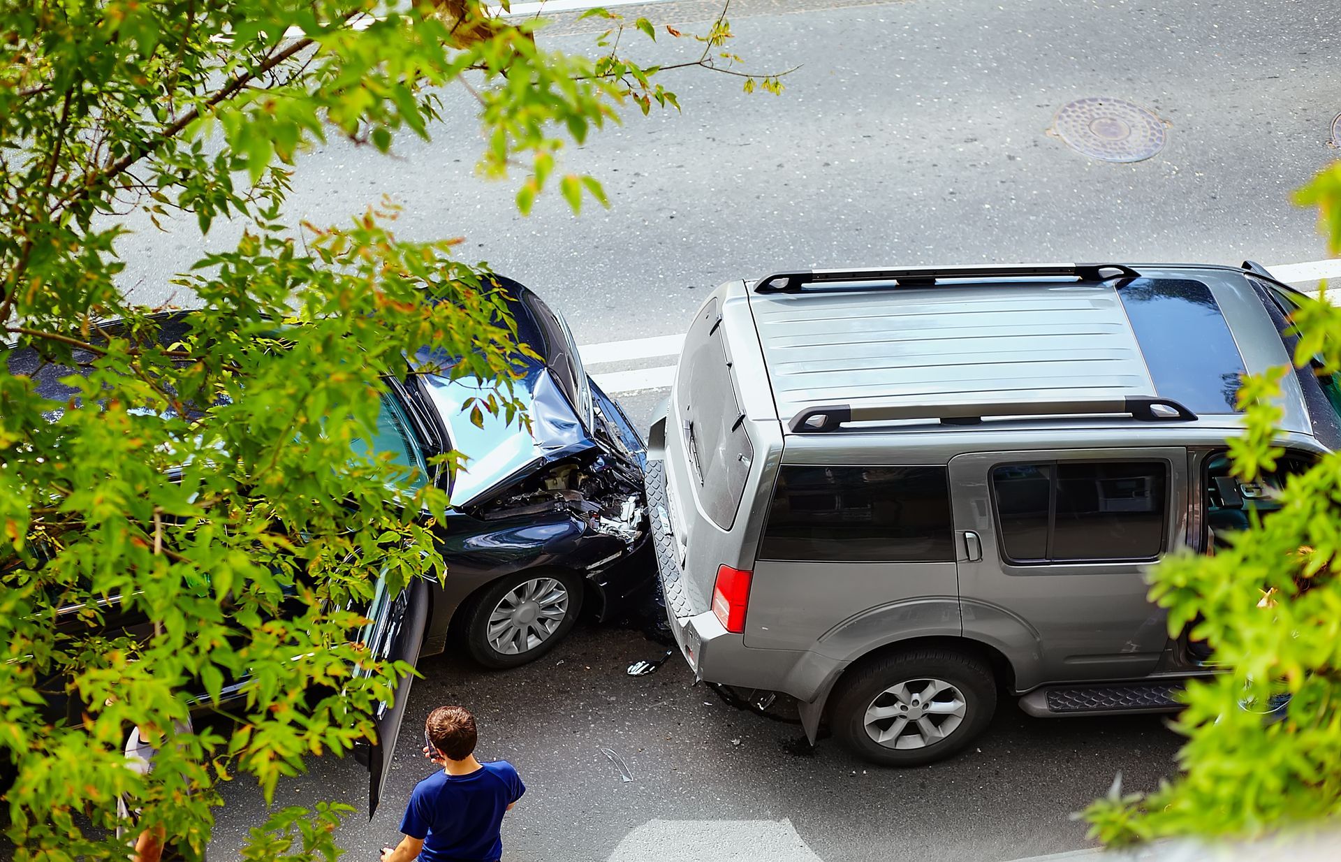 Damaged black car involved in a traffic accident, debris on the road, other cars in the background.