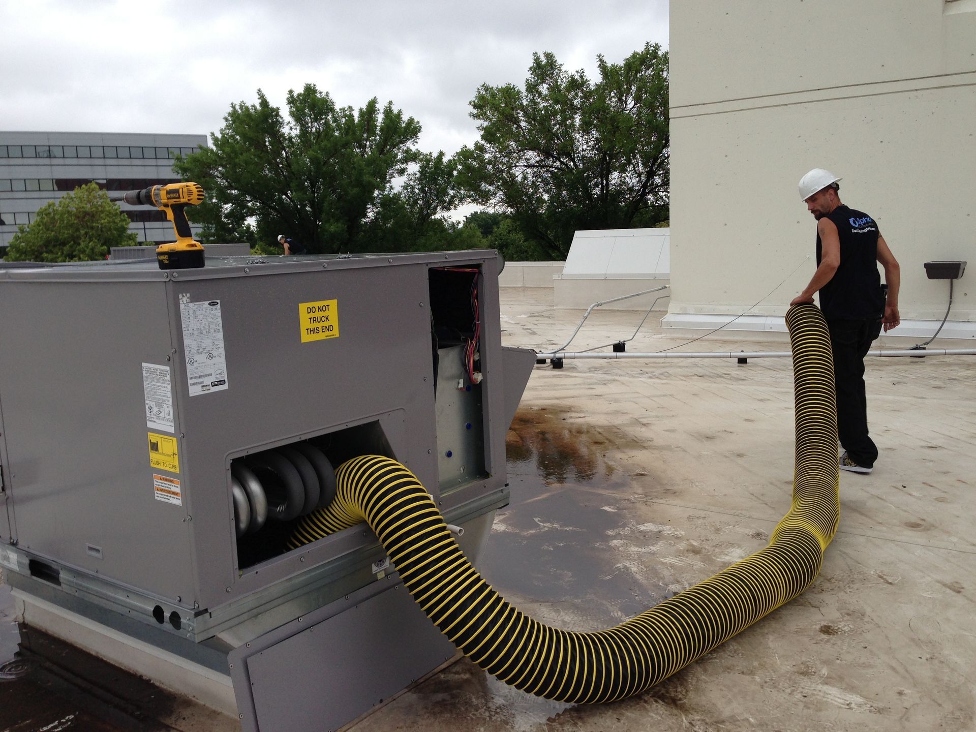 Alpha Air Corporation technician on a rooftop connects a yellow and black flexible duct to an air handler.