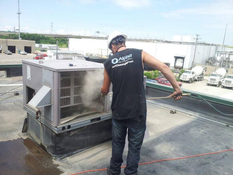 Person in hard hat cleaning rooftop HVAC unit with steam.