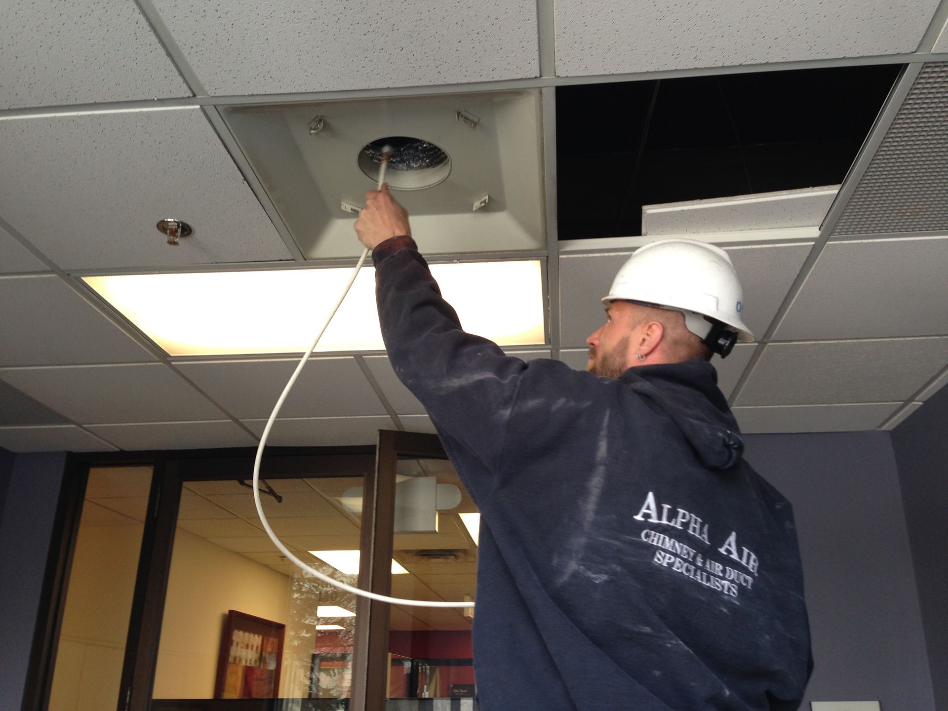 Alpha Air Corporation technician examining ceiling ventilation with a probe.