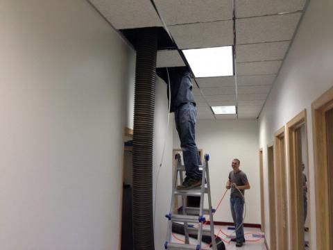 Person on ladder, working on ceiling in hallway. Another person watches.
