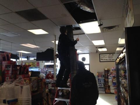 Men on a ladder working on a ceiling in a store, light fixtures and products visible.