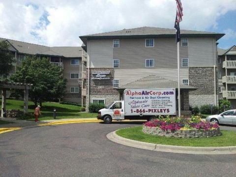 White service truck parked in front of a multi-story building with a small flower bed and an American flag.