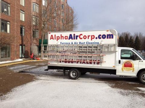 White Alpha Air Corp truck parked near a building, carrying ladders and snow on the ground.