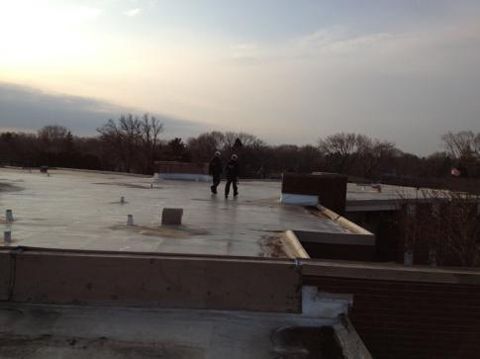 Two people on a flat roof under a cloudy sky. They are standing near a brick chimney.