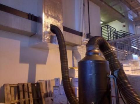 Large industrial dust collector with flexible hoses attached to a duct and a wall.