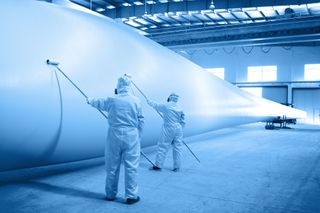 Two men are painting a large white object in a factory.