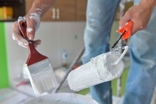 A person is holding a paint brush and a paint roller.