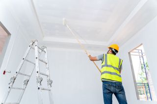 A man is painting the ceiling of a room with a roller.