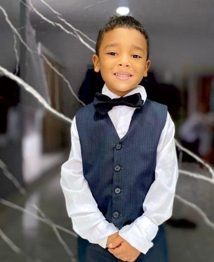 Niño pequeño con traje formal, sonriente, con pajarita y chaleco.