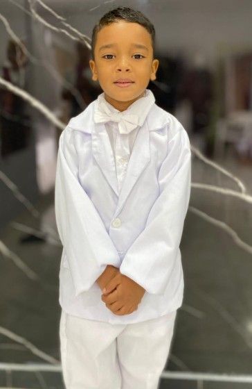 Niño con traje blanco y pajarita, de pie en un espacio bien iluminado.