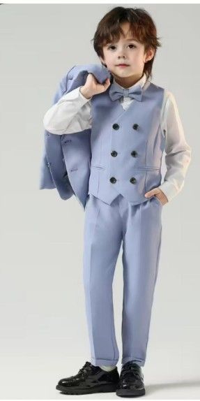 Niño con traje azul claro sosteniendo una chaqueta, mirando a la cámara.