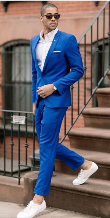 Hombre con traje azul, camisa blanca, zapatillas deportivas y gafas de sol, bajando unas escaleras.