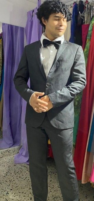Man in a dark suit with a bow tie. He is standing inside a store with colorful clothing.
