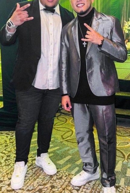 Dos hombres con traje posando en interiores, uno de negro y el otro de plateado metalizado; ambos con zapatillas deportivas