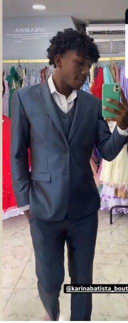 Una persona con traje azul se mira en un espejo mientras sostiene un teléfono. Está en una tienda de ropa.