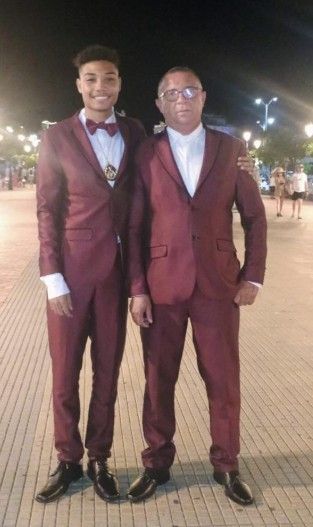 Dos personas con trajes burdeos a juego están juntas al aire libre por la noche.