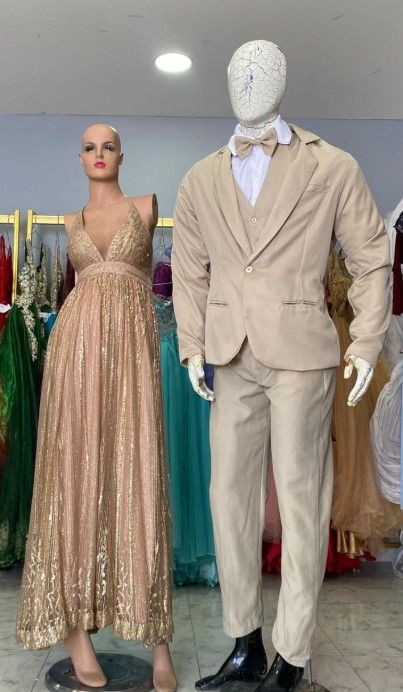 Mannequins in formal wear: a shimmering gold gown and a tan suit, displayed in a shop.