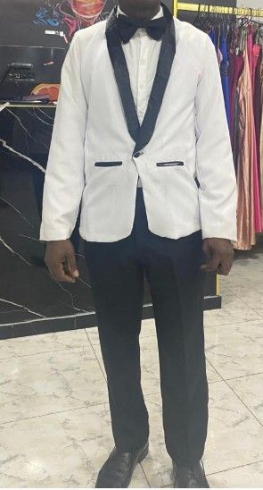 Persona con chaqueta de esmoquin blanca con solapas negras y pajarita, pantalones negros, en una tienda de ropa.