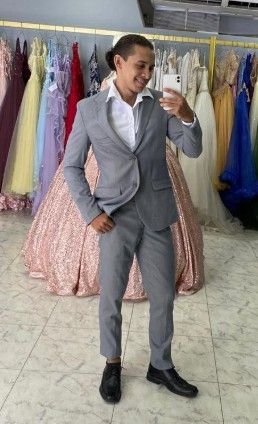 Hombre con traje gris tomándose una selfie en una tienda de vestidos, con vestidos al fondo.