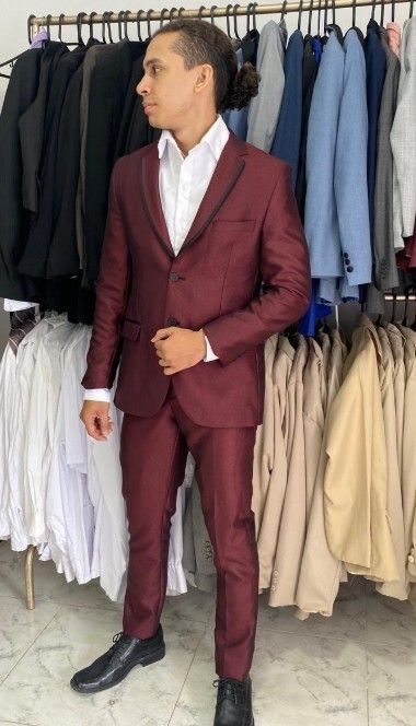 Hombre con traje burdeos y camisa blanca, de pie en una tienda de ropa, mirando hacia otro lado.