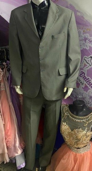 Maniquí vestido con traje gris y camisa negra, en una tienda de ropa con vestidos.