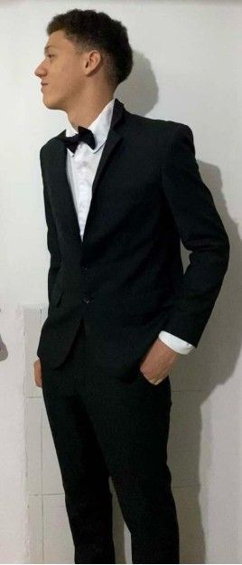 Hombre con traje negro y pajarita, manos en los bolsillos, posando de perfil.