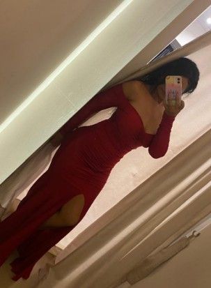 Mujer con vestido rojo de hombros descubiertos y abertura alta, tomándose una selfie frente al espejo.