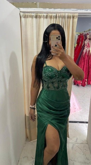 Mujer con vestido verde, corpiño con cuentas y abertura en la pierna, tomándose una selfie frente al espejo.