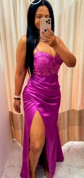 Mujer con un vestido rosa con una abertura hasta el muslo, tomándose una selfie en el espejo.