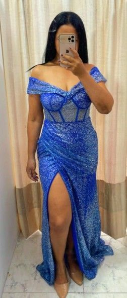 Mujer con vestido azul de lentejuelas con hombros descubiertos y abertura alta, sosteniendo un teléfono