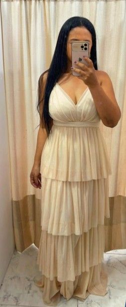 Mujer con un vestido formal de capas color crema, tomándose una selfie frente al espejo, delante de una cortina.