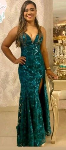 Mujer con un vestido de lentejuelas color verde azulado, sonriendo, de pie junto a una mesa con la mano en la cadera.