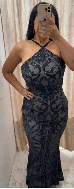 Mujer con un vestido largo negro de cuello halter y con elaborados abalorios, posando en un probador.