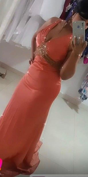 Mujer con un vestido naranja con aberturas, sosteniendo un teléfono, de pie en el interior.