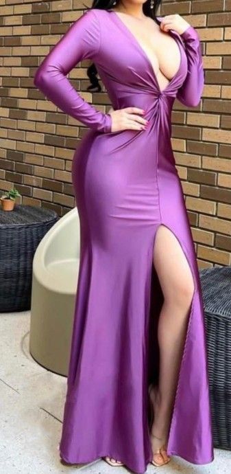 Mujer con un vestido largo morado con una abertura hasta el muslo, posando al aire libre cerca de una pared de ladrillos.