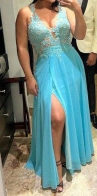 Mujer con un vestido azul claro con una abertura alta, sosteniendo un teléfono, de pie en el interior.