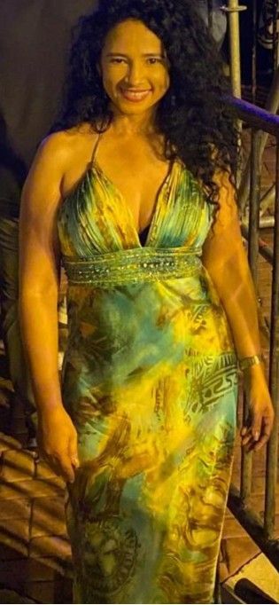 Mujer con vestido halter sonriendo, de pie al aire libre. El vestido es verde y amarillo. Cabello oscuro y rizado.