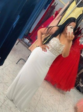 Mujer con vestido formal blanco, tomándose una selfie frente al espejo en una tienda de vestidos.