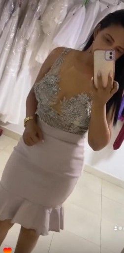 Mujer con top sin mangas y falda lápiz tomándose una selfie en el espejo de una tienda de vestidos.