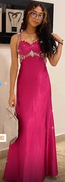 Mujer con un vestido magenta con corpiño enjoyado, sosteniendo un pequeño bolso plateado, posando.