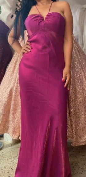 Mujer con un vestido magenta de cuello halter y abertura hasta el muslo, posando en una tienda con otros vestidos.