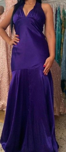 Mujer con un vestido halter de satén morado posando, con la mano en la cadera, en una tienda de vestidos.