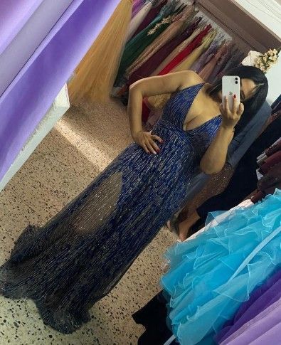 Mujer con un vestido azul marino de lentejuelas posando frente a un espejo, con la mano en la cadera. 