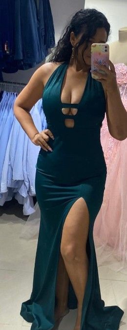 Mujer con un vestido halter verde oscuro con una abertura alta, sosteniendo un teléfono, en una tienda de ropa.